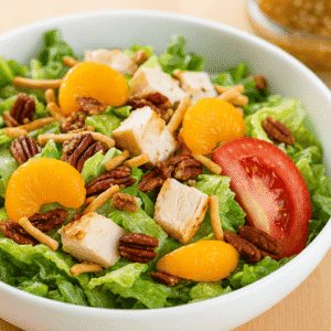 A salad with Romaine lettuce, grilled chicken breast, Mandarin oranges, chopped pecans, crispy noodles, tomato, Asian sesame dressing.